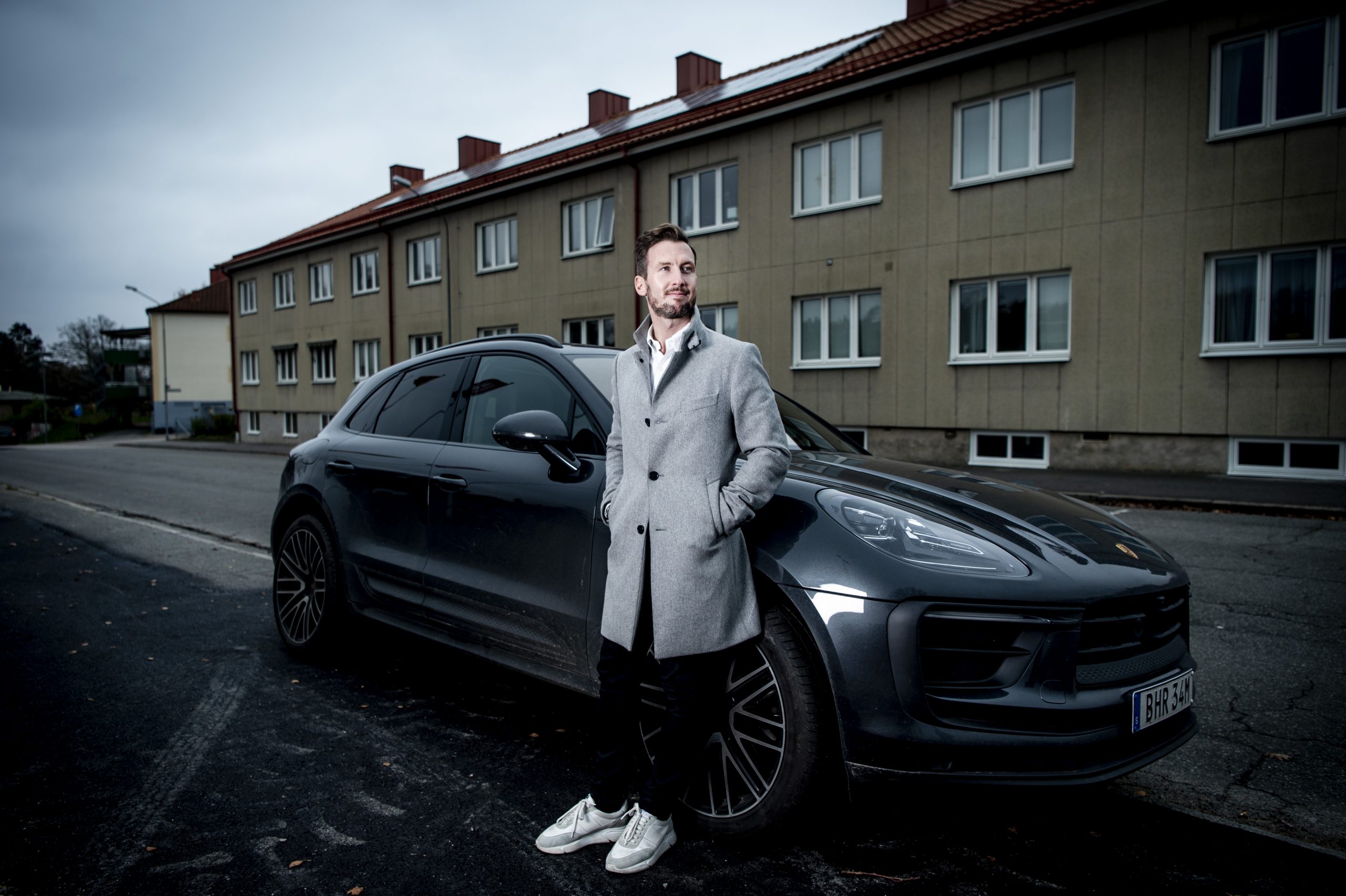 man i överrock framför porsche